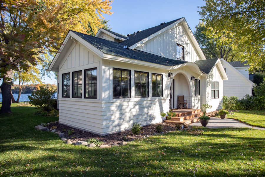 White lakeside home remodel: sunroom, dark roof, black windows, arched wood steps.