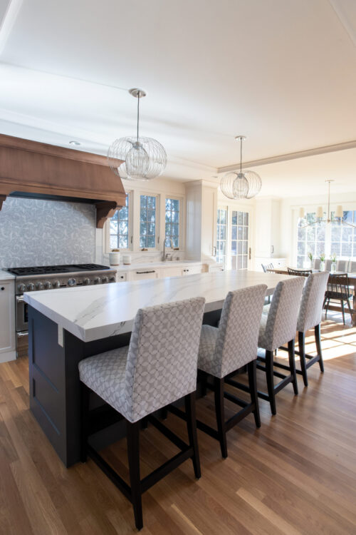 Kitchen remodel features large quartz island, natural wood floors, white cabinetry, modern pendants.
