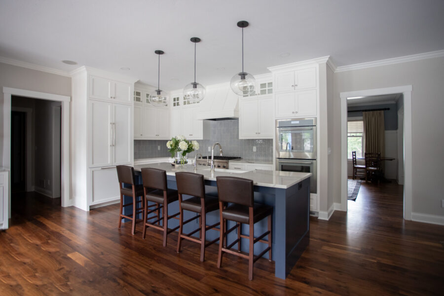 Twin Cities kitchen remodel features white cabinetry, a blue island, grey tile backsplash, and wood floors.
