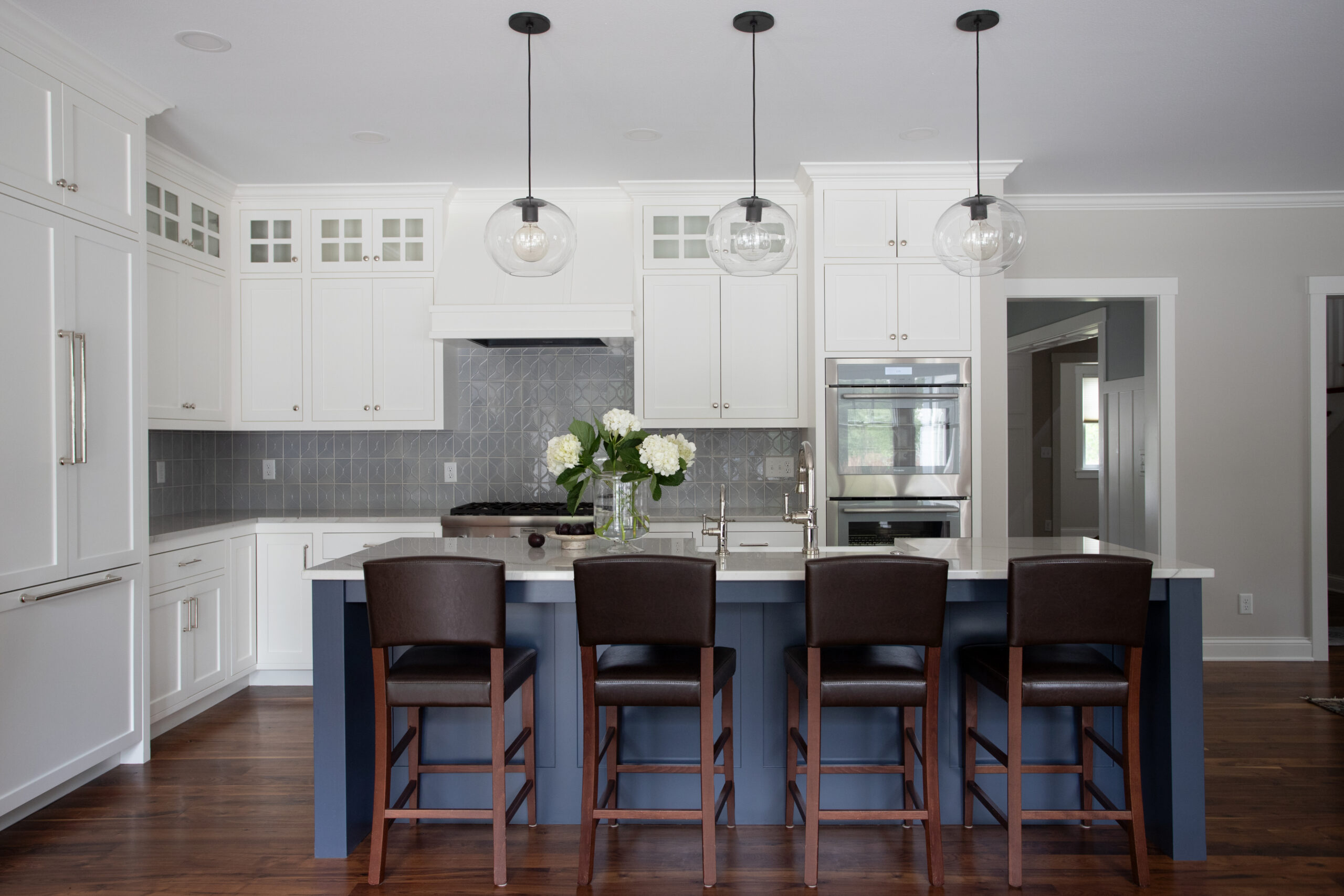 A modern kitchen remodel features white shaker cabinets, a blue island with seating, dark wood floors, and pendant lights. Twin Cities.