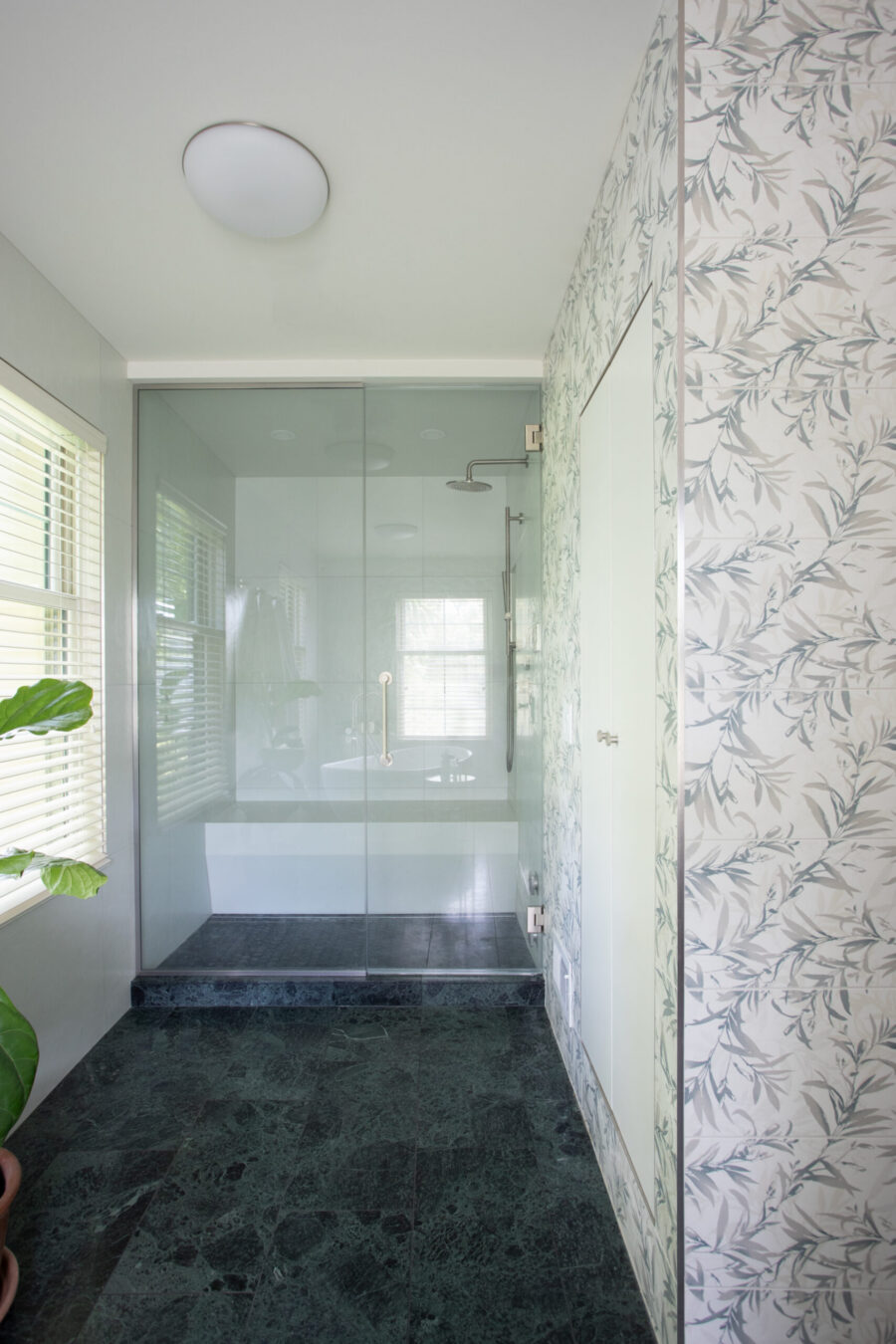 This Twin Cities bathroom remodel features a glass shower, dark green marble floor, and leaf-patterned wall tiles.