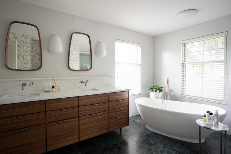Modern bathroom renovation incorporates dark wood vanity, marble, and a freestanding tub.