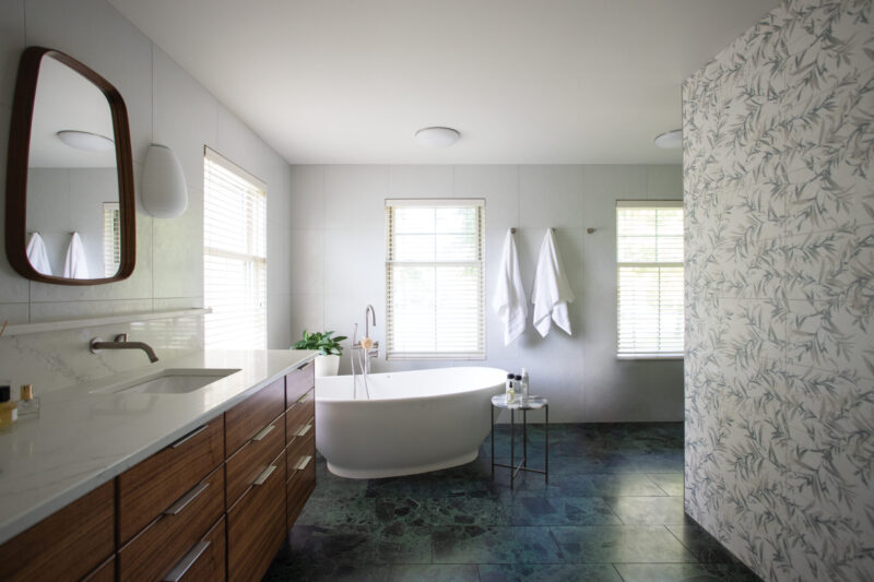 Modern bathroom renovation: wood vanity, freestanding tub, dark-tiled floor.