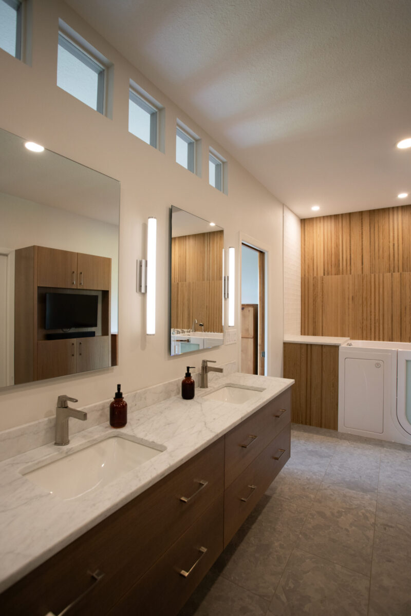 Twin Cities bathroom remodel features a floating wood dual vanity with marble counter, slatted wood wall, and walk-in tub.