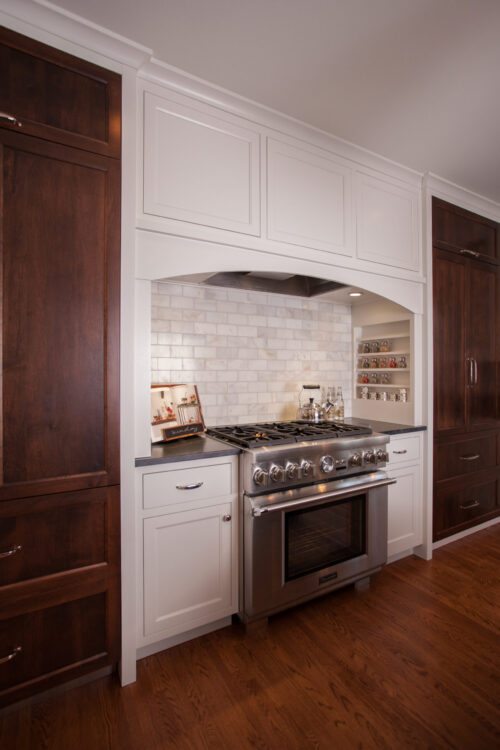 White cabinetry frames stainless-steel range beneath arched-hood marble-tile-backsplash