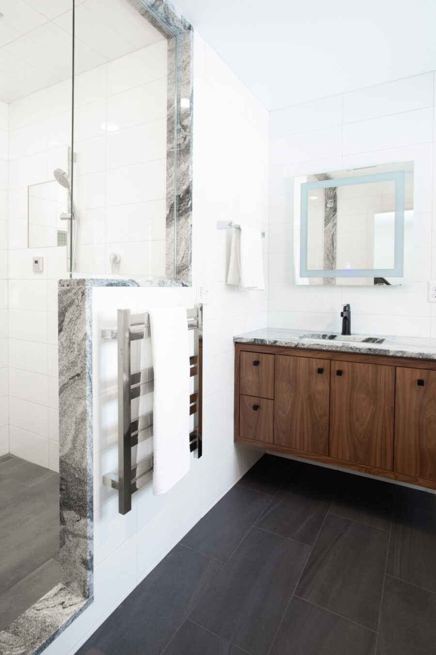 Modern Twin Cities bathroom renovation features white tile, dark floor, wood vanity, and granite shower.