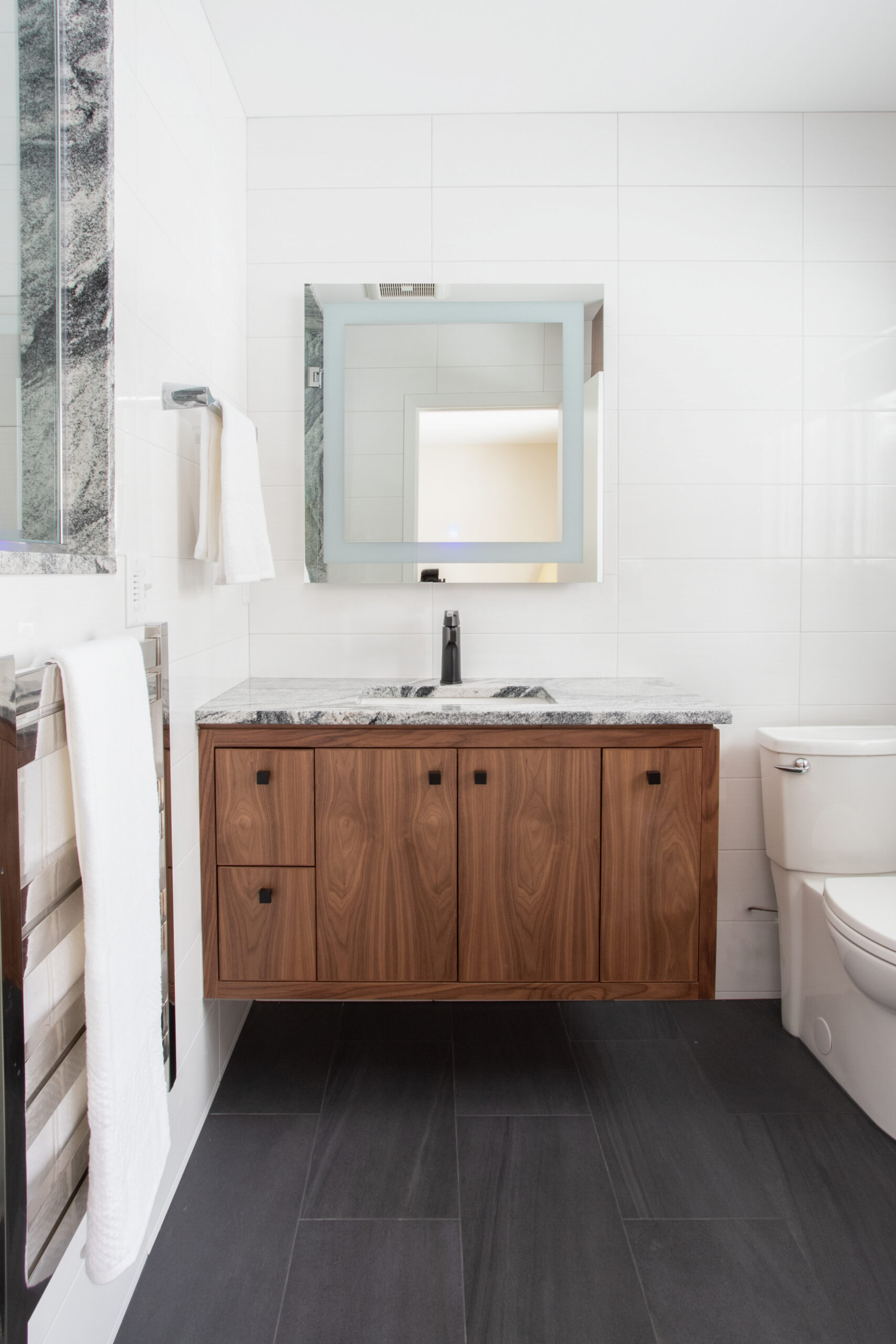 Modern Twin Cities bathroom remodel features floating wood vanity, granite, white walls, dark floor tiles.