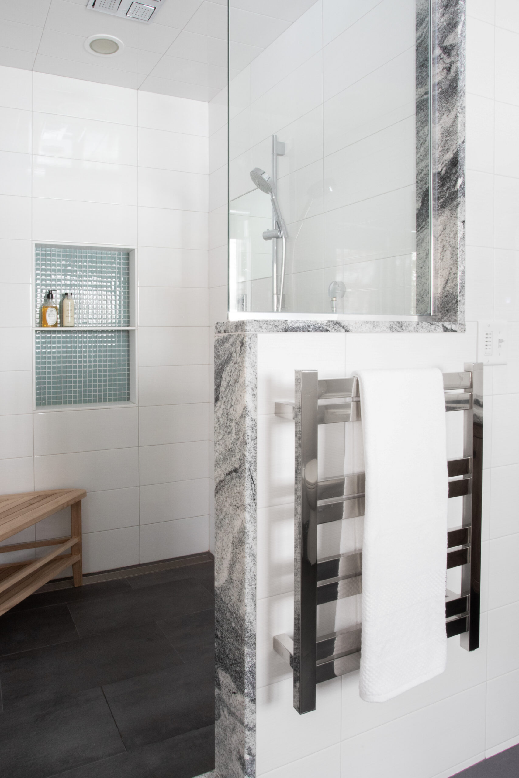 Clean modern bathroom renovation: white tiles, dark floor, granite, shower, towel warmer.