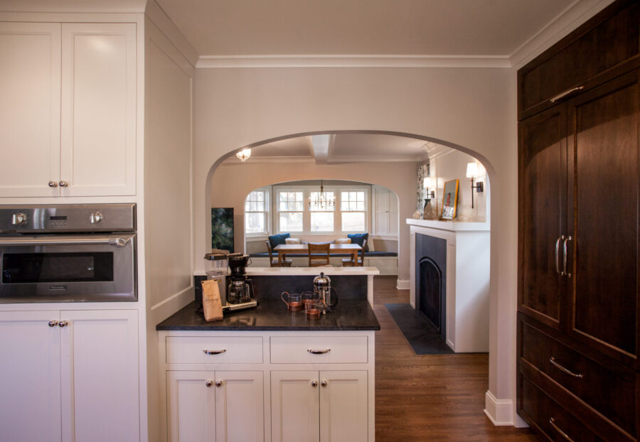 Bright kitchen renovation presents white cabinetry, dark countertops, arched dining room.