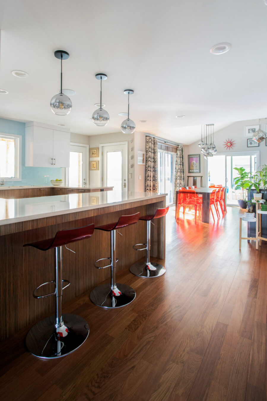 Modern kitchen-dining remodel features wood floors, white counters, red barstools.