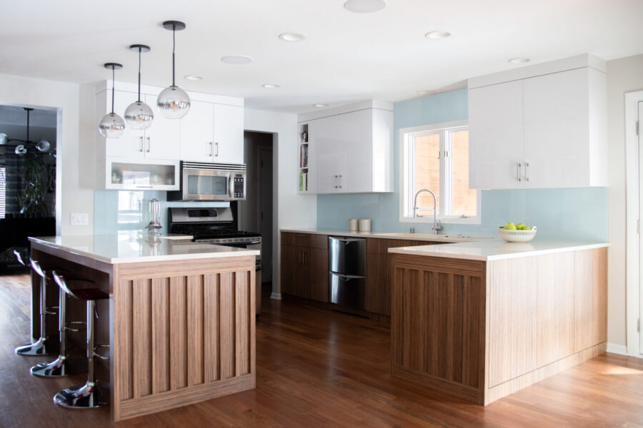 Kitchen renovation features glossy-white cabinetry, wood-paneled islands, glass backsplash.