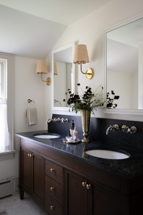 Twin Cities bathroom remodel: dark wood double vanity, black marble, brass sconces, and bright mirrors.