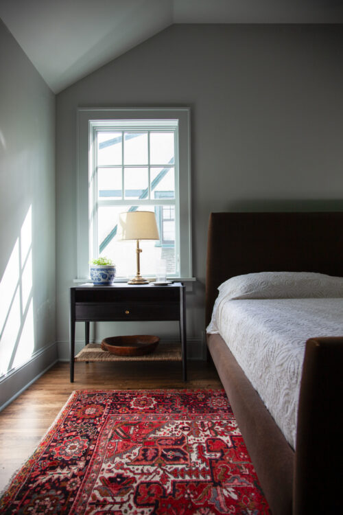 Updated Twin Cities bedroom design features sloped ceiling, dark furnishings, hardwood flooring.