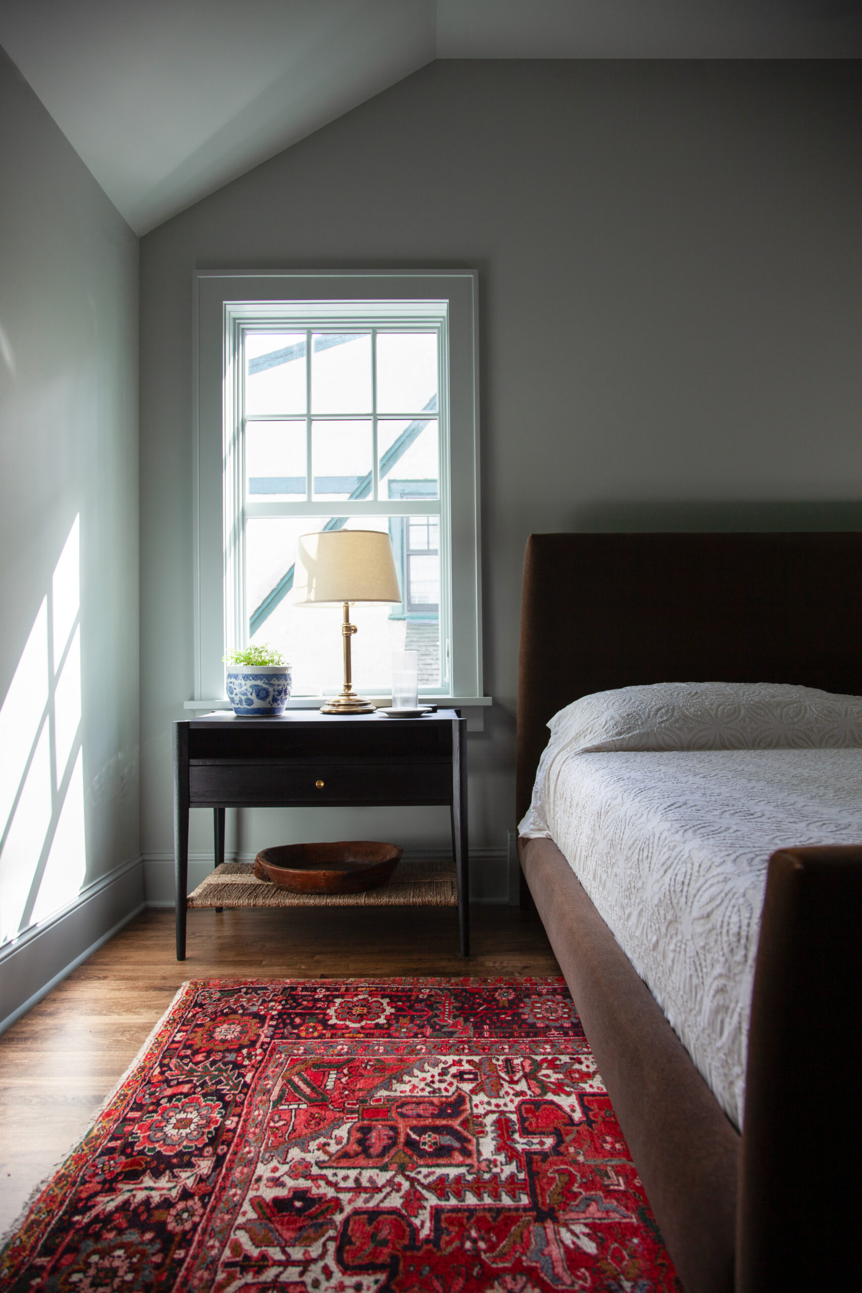 Updated Twin Cities bedroom design features sloped ceiling, dark furnishings, hardwood flooring.