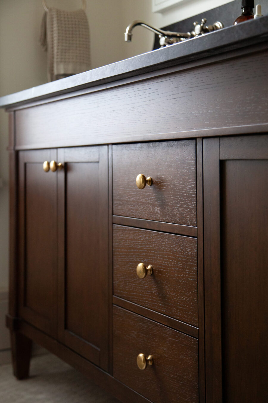 Dark wood vanity offers stone countertop, brass hardware, elegant bathroom-remodel design.