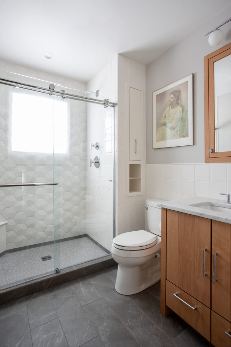 Bright Twin Cities bathroom remodel features glass shower, wood vanity, gray tile floor.