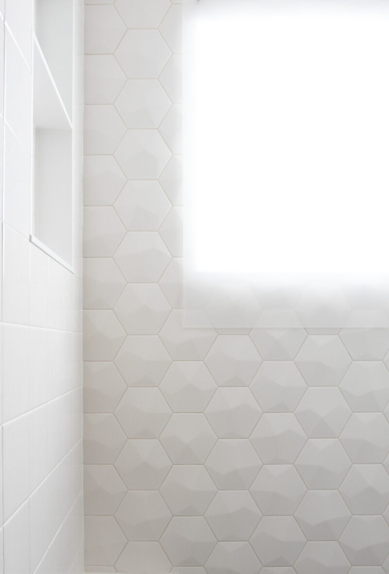 Bright white bathroom remodel features textured hexagonal tiles, built-in niche. Twin Cities.