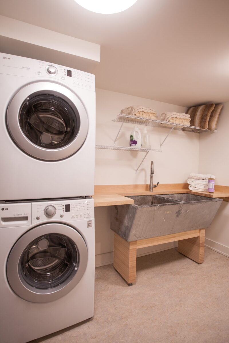 Modern laundry renovation. Stacked appliances, wood counter, metal sink.