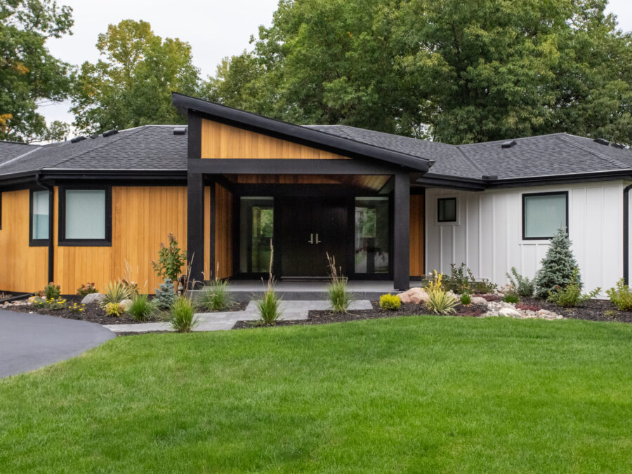Modern home renovation highlights natural wood, vertical white siding, black architectural trim.
