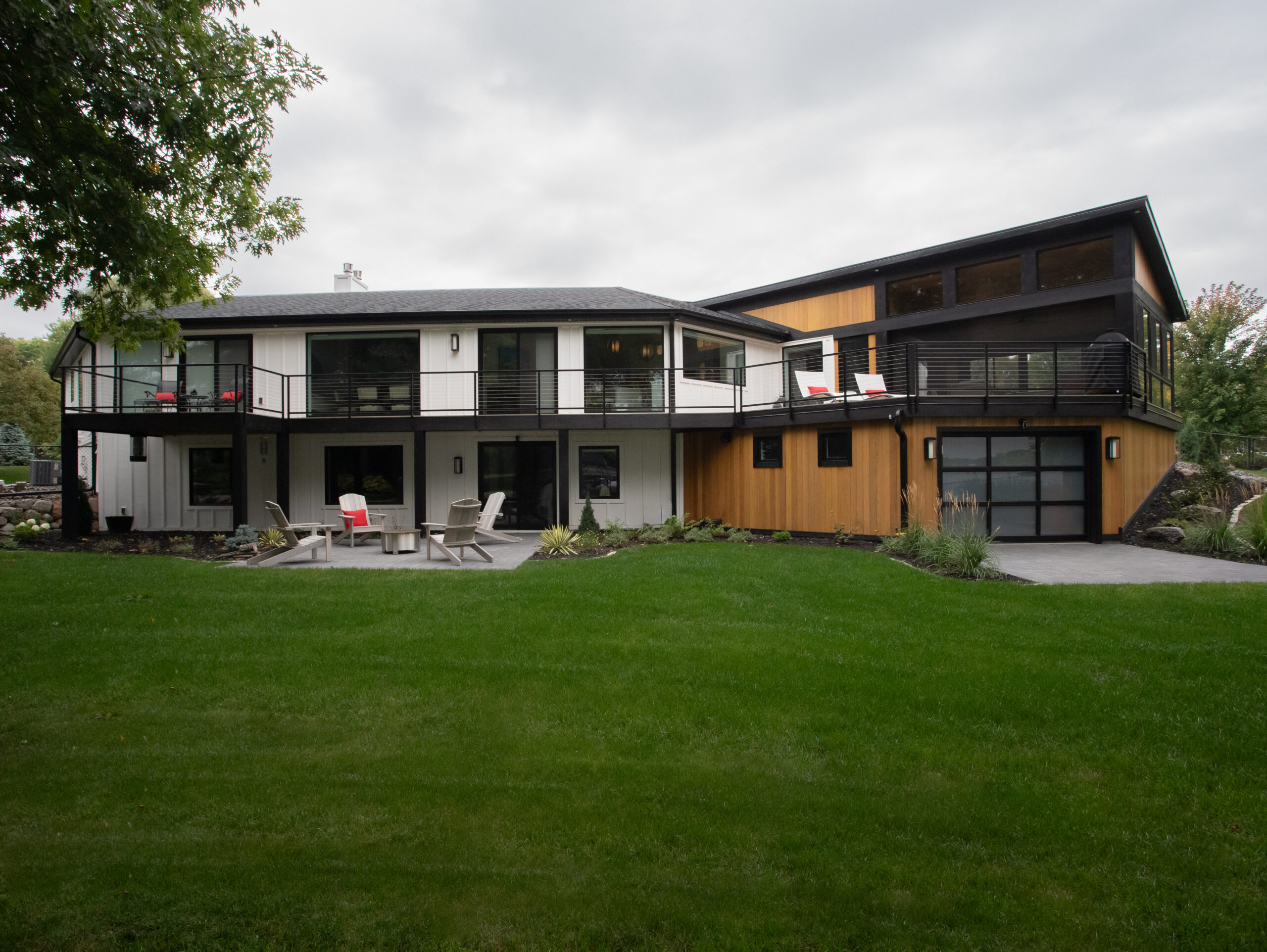 Modern home renovation combines white siding, wood panels, black accents, lush landscaping.