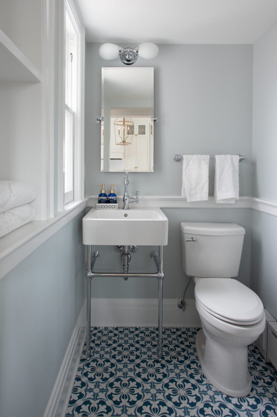 Twin Cities bathroom remodel updates with a console sink, toilet, blue patterned floor tile, light walls, chrome fixtures.