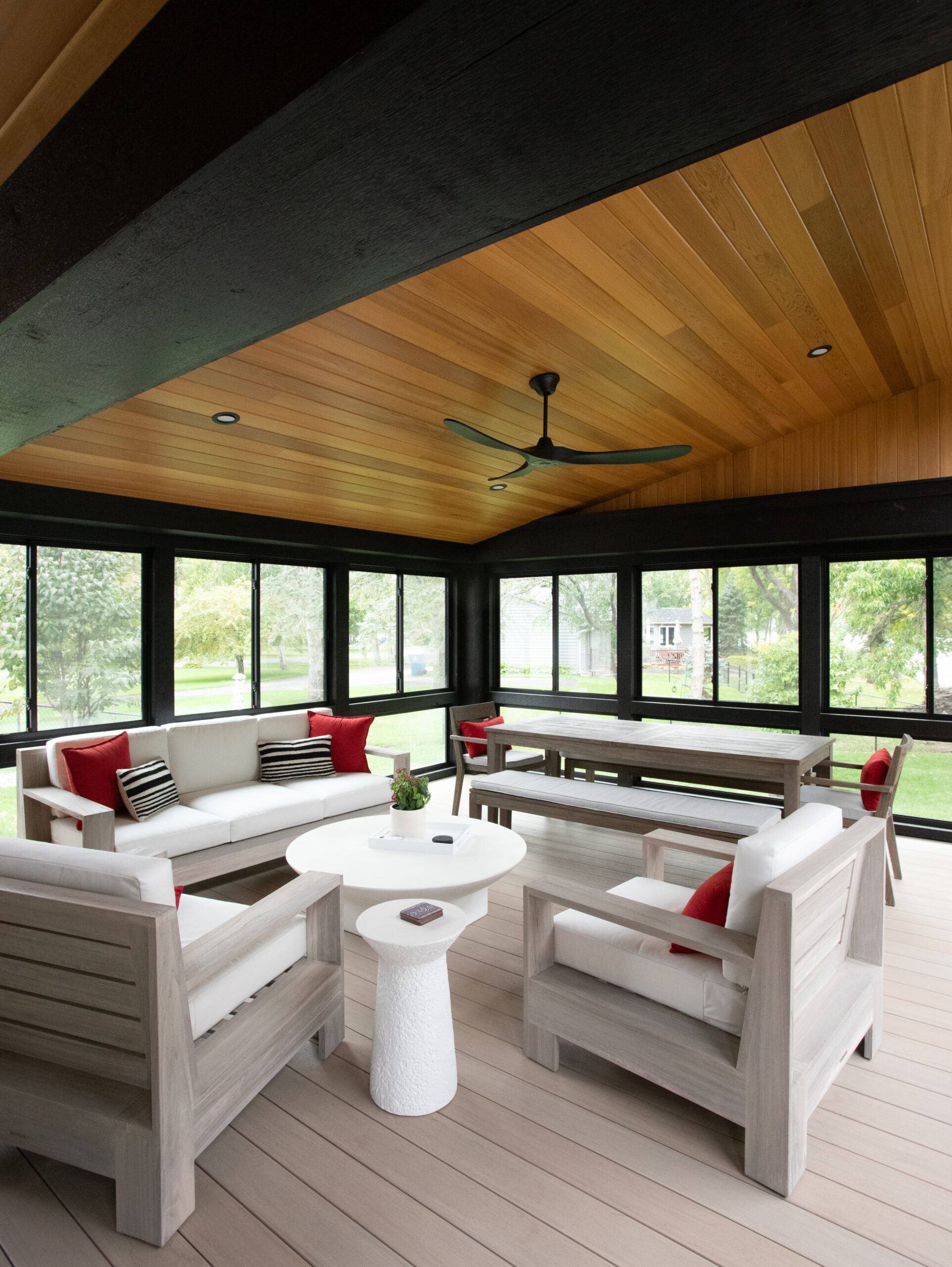 Modern Twin Cities sunroom design features a wood plank ceiling, dark window frames, and light grey outdoor furniture.