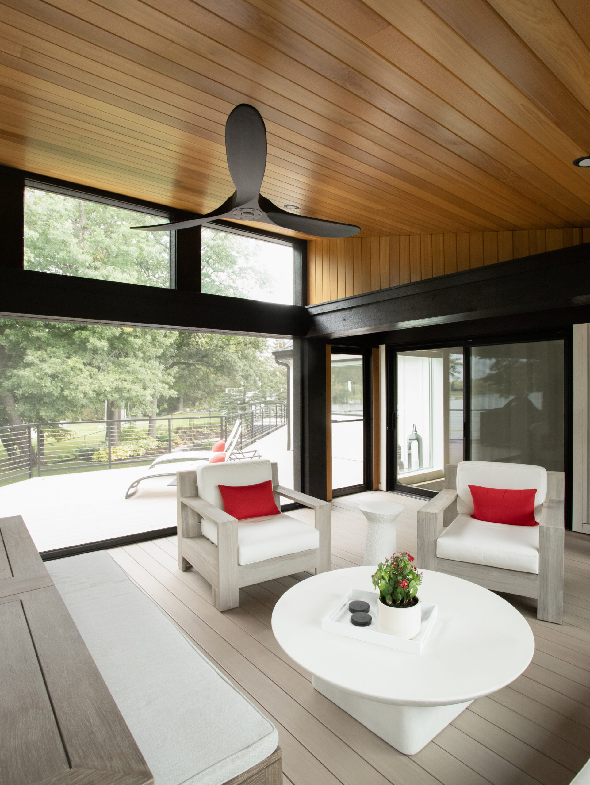 Modern home renovation outdoor living space features wood ceiling, dark beams, large windows.