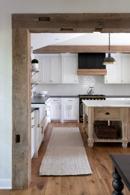 Twin Cities kitchen remodel features rustic wood beams, white shaker cabinets, dark countertops, and a bright island with pendant lighting.
