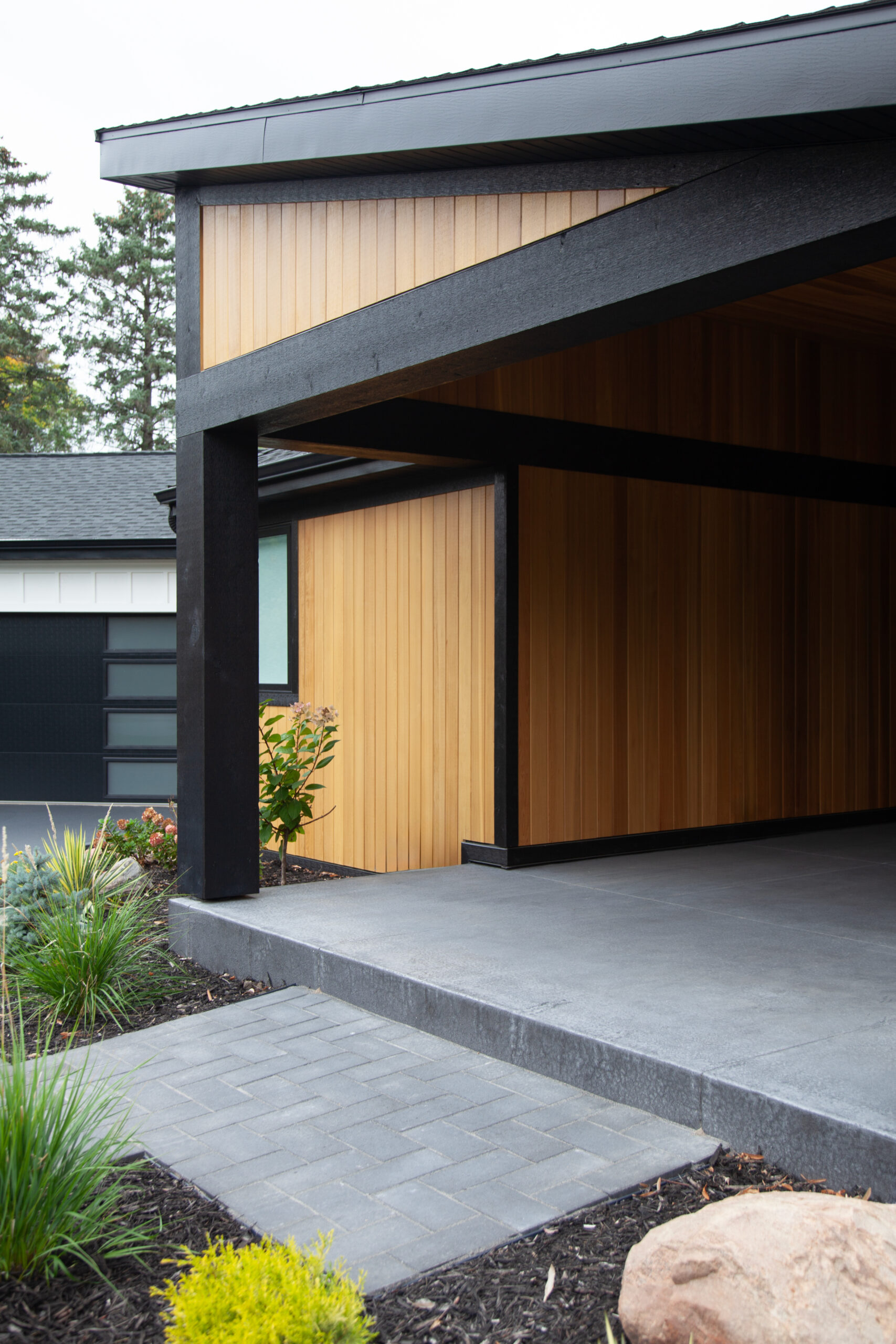 Charcoal-coated structural-beams frame warm-natural cedar-cladding over broad-textured concrete-porch