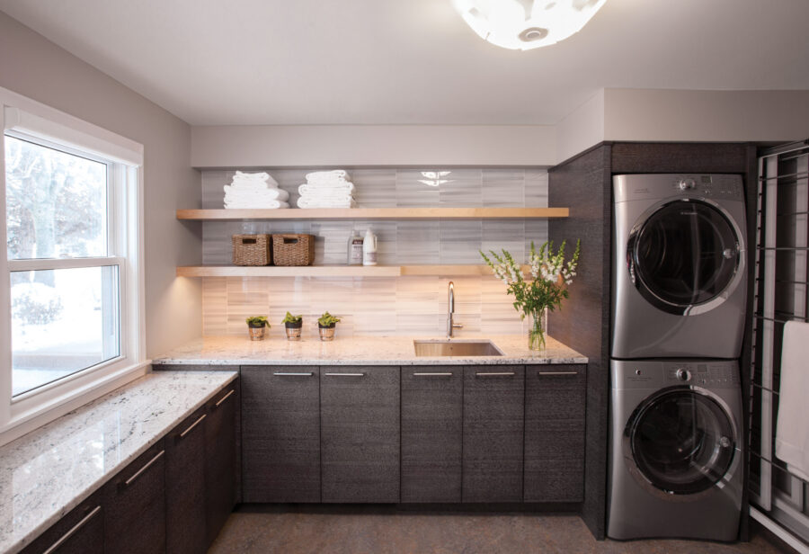 Sleek Twin Cities laundry room features dark cabinetry, light granite, stacked appliances.