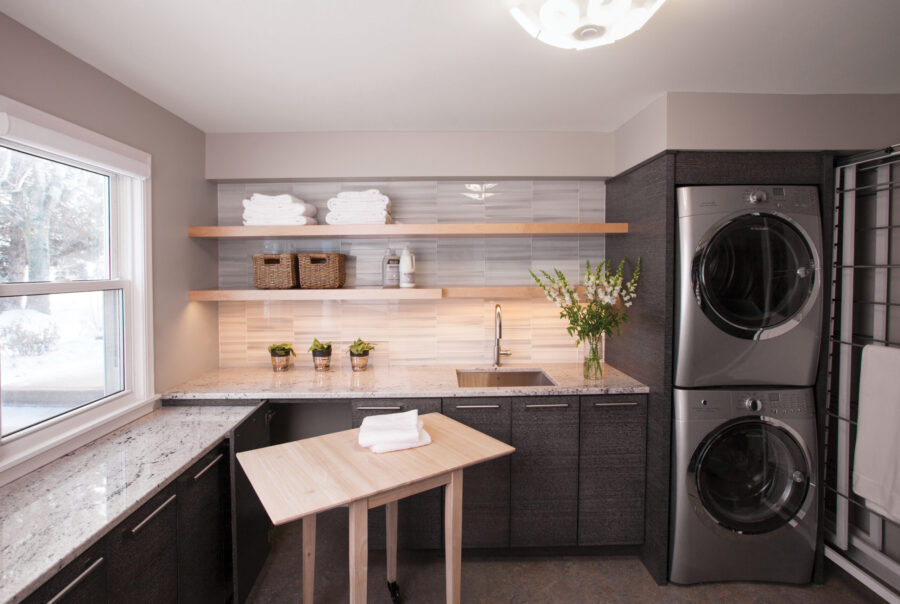 Modern Twin Cities laundry room renovation offers stacked machines, dark cabinets, granite counters, and warm lighting.