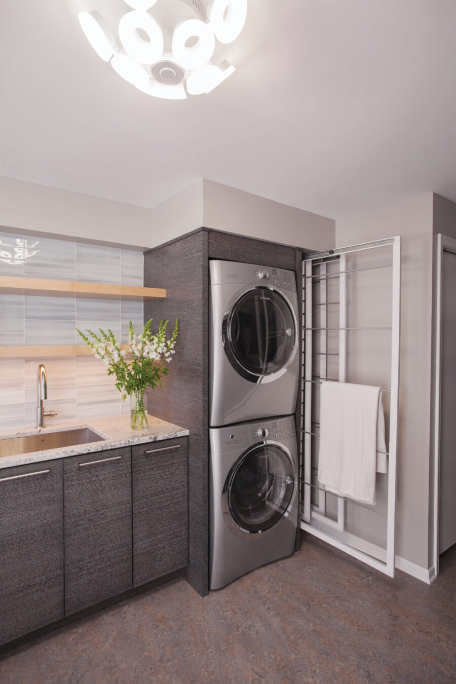 Modern Twin Cities laundry room remodel highlights stacked grey appliances, dark cabinets, stone counters, and light tile backsplash.