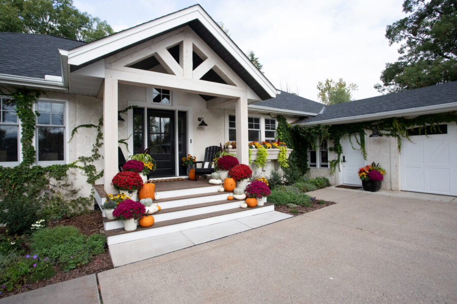 Remodeled stucco residence displays craftsman porch, dark door, seasonals.