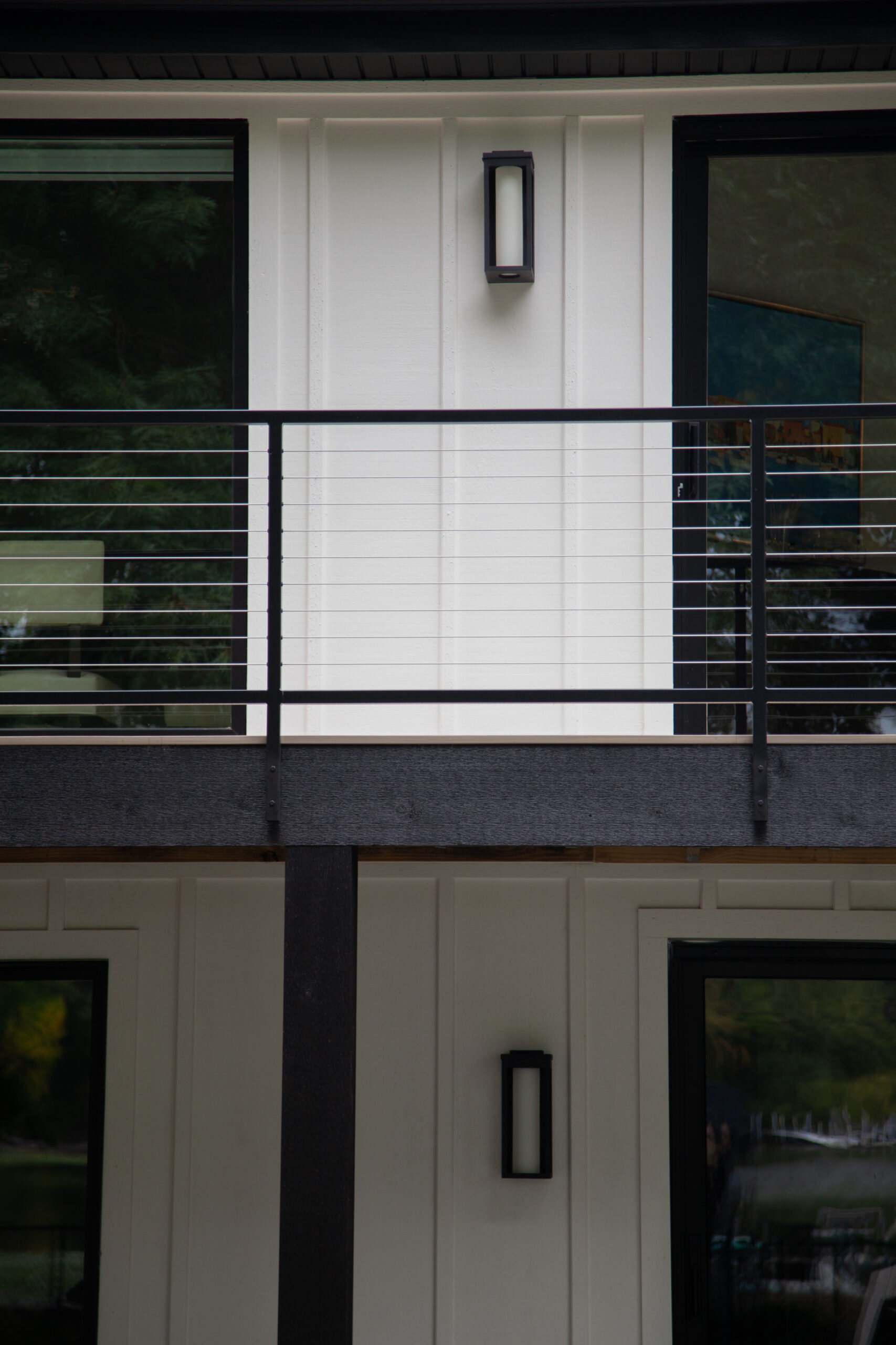 Facade has white-board-and-batten-siding black-steel-cable-railing rectangular-wall-sconces dark-framed-windows