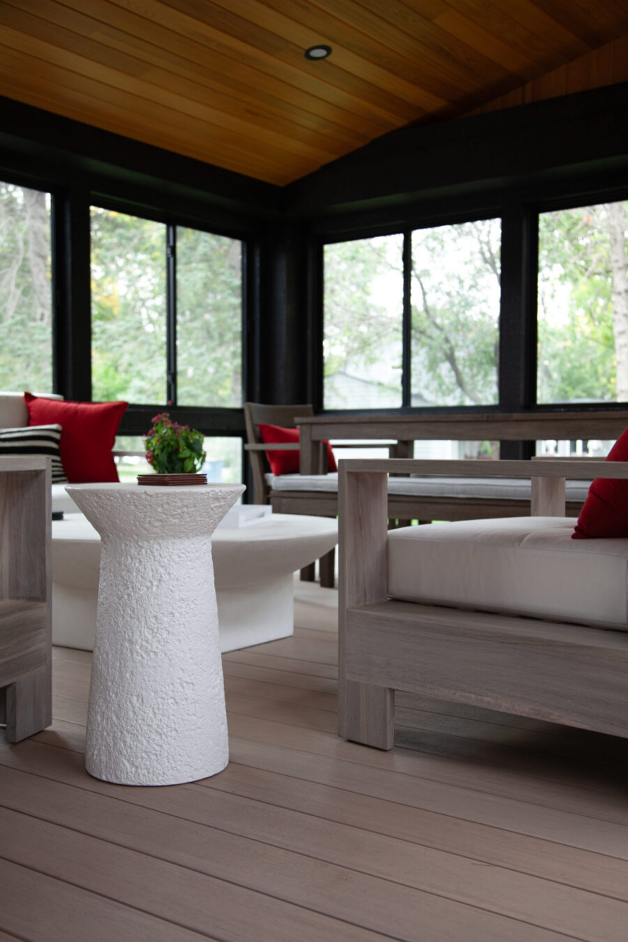 Modern screened porch features wood ceiling, light floor, large windows. Contemporary furniture ideal for home renovation.