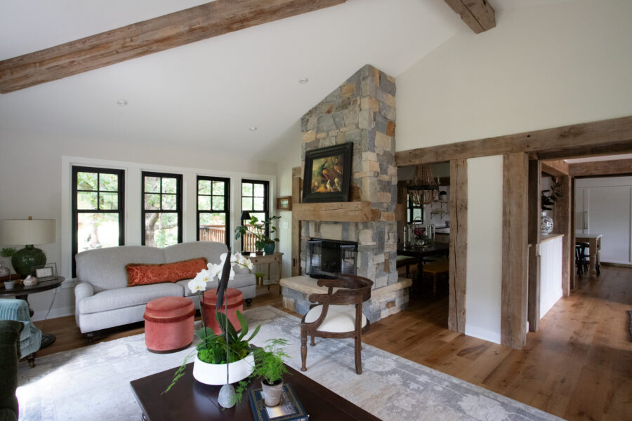 Renovated Twin Cities living room boasts prominent stone fireplace, rugged wood beams, large windows.