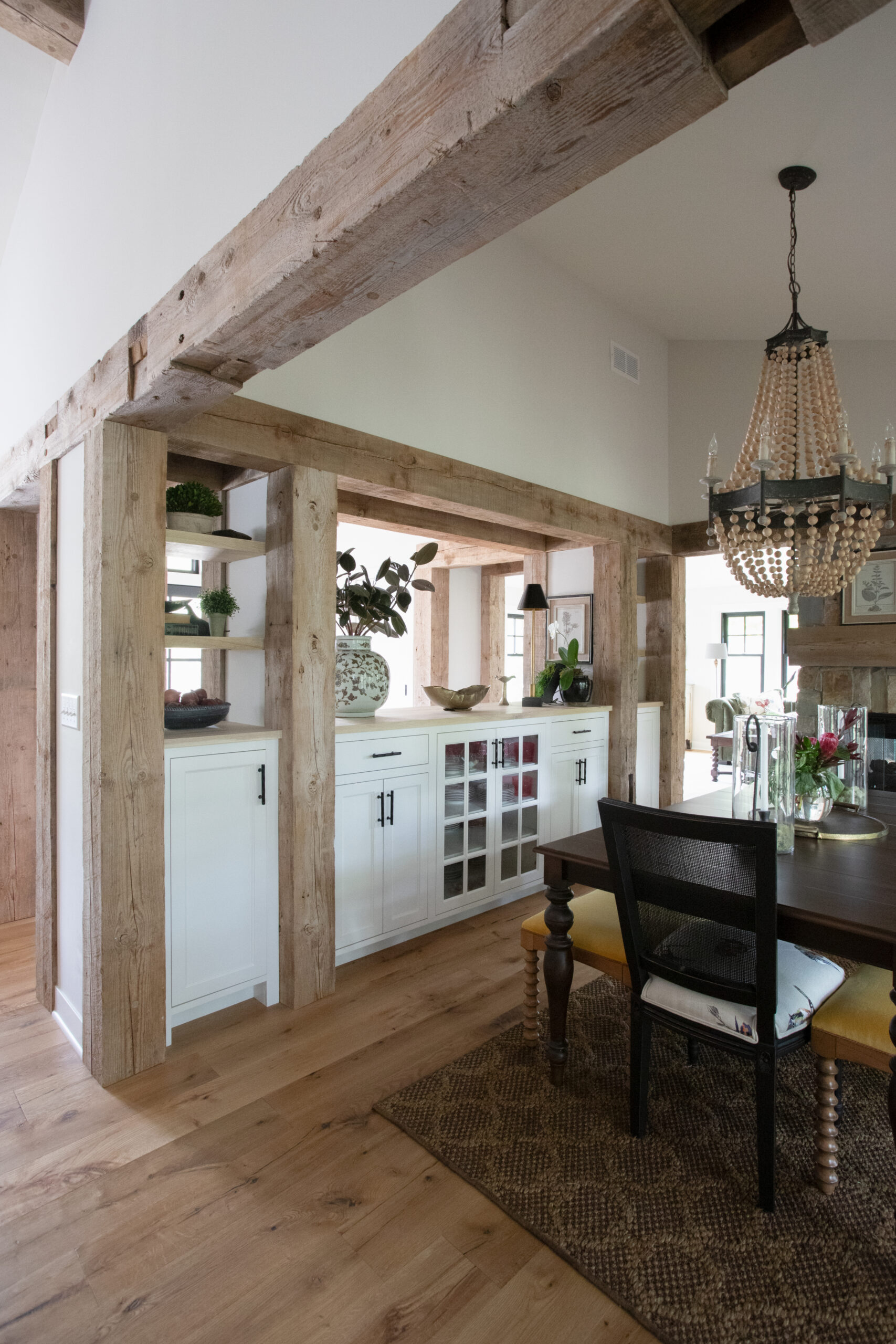 Reclaimed-timber beams structurally anchor farmhouse dining with handcrafted-millwork cabinetry.