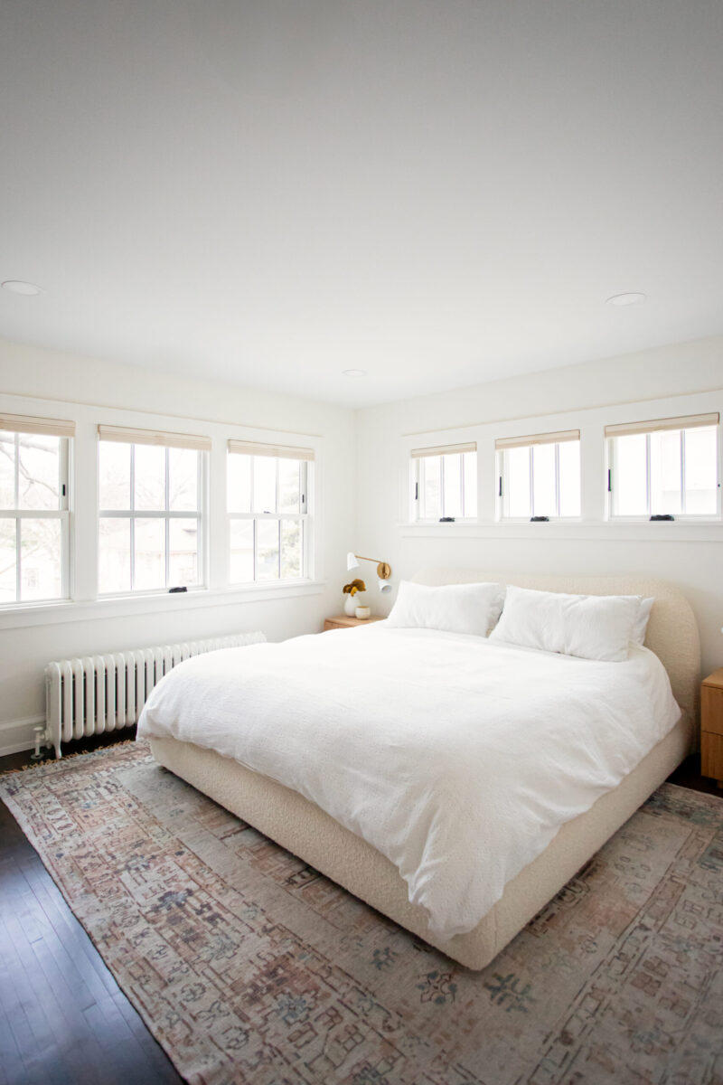 Twin Cities bedroom remodel features white bouclé bed, dark wood floors, bright windows.