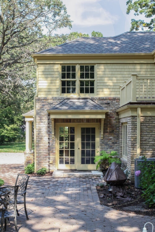 Sunlit two-story yellow-shingled brick-clad residence features multi-pane French doors