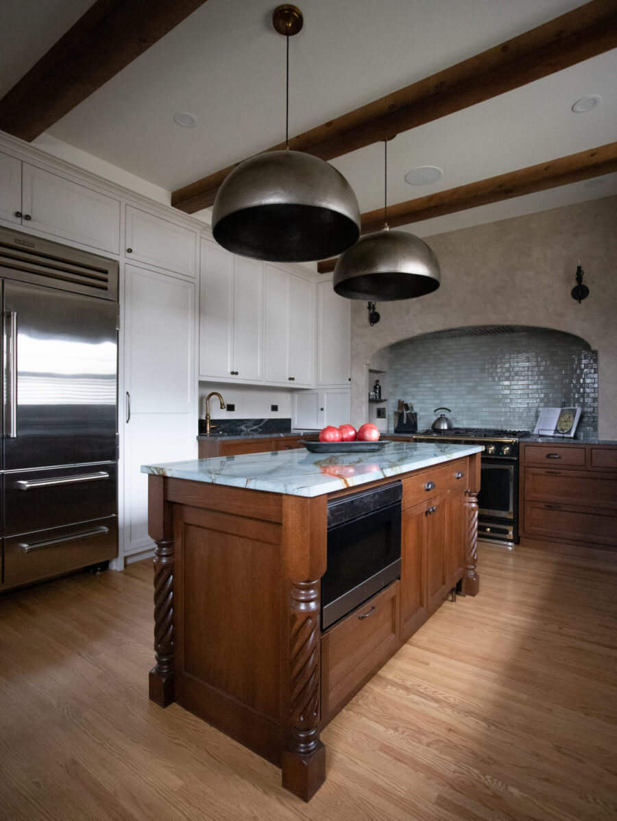 Sophisticated kitchen remodel features white-paneled cabinetry, carved-wood island, metallic pendant lights.