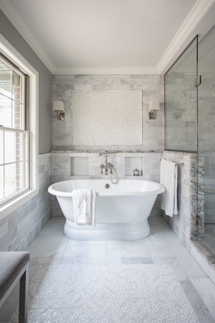 Elegant Twin Cities bathroom renovation features a freestanding tub, marble walls, a glass shower, and geometric floor mosaic.