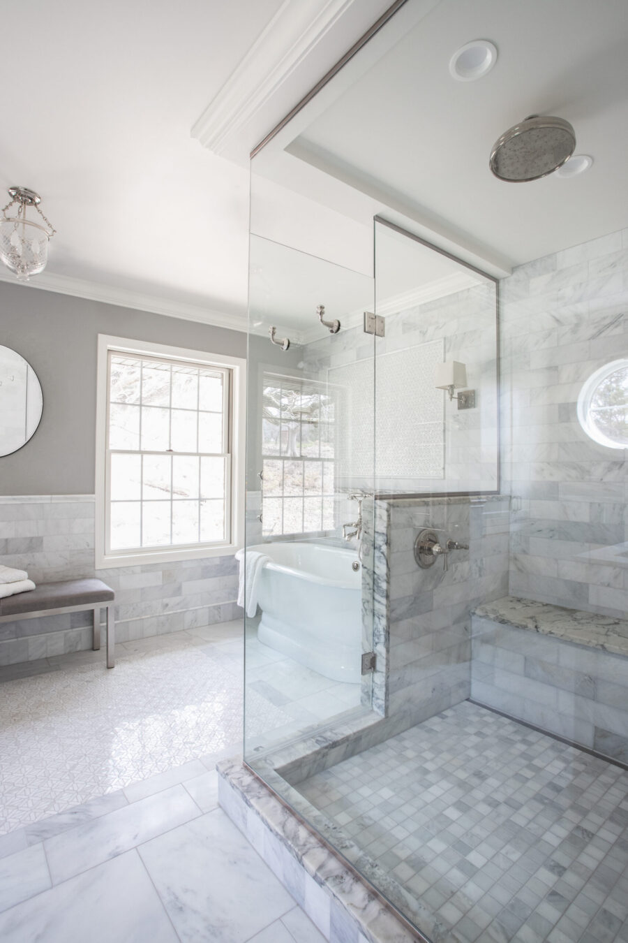 Bright Twin-Cities bathroom-remodel boasts marble-walls, glass-shower, freestanding-tub, two-windows.