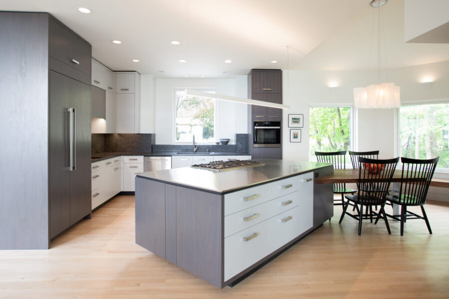 Modern kitchen remodel. Two-tone cabinetry, dark counters, light wood floor. Island with cooktop and dining. Twin Cities.