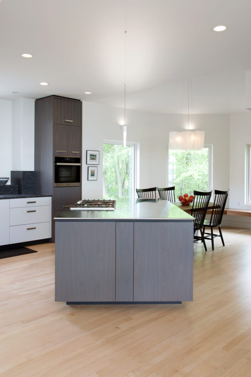 A bright kitchen remodel in Twin Cities provides a large gray island, dark cabinets, light wood floors, and ample natural light.