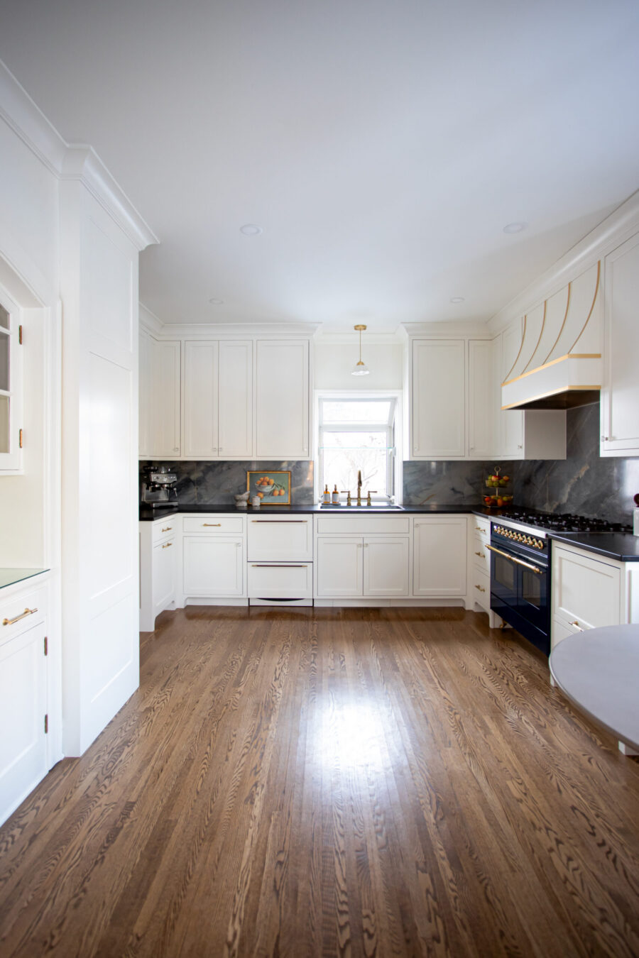 White shaker cabinets, dark marble backsplash, black counters, and hardwood floors define this kitchen remodel. Twin Cities.