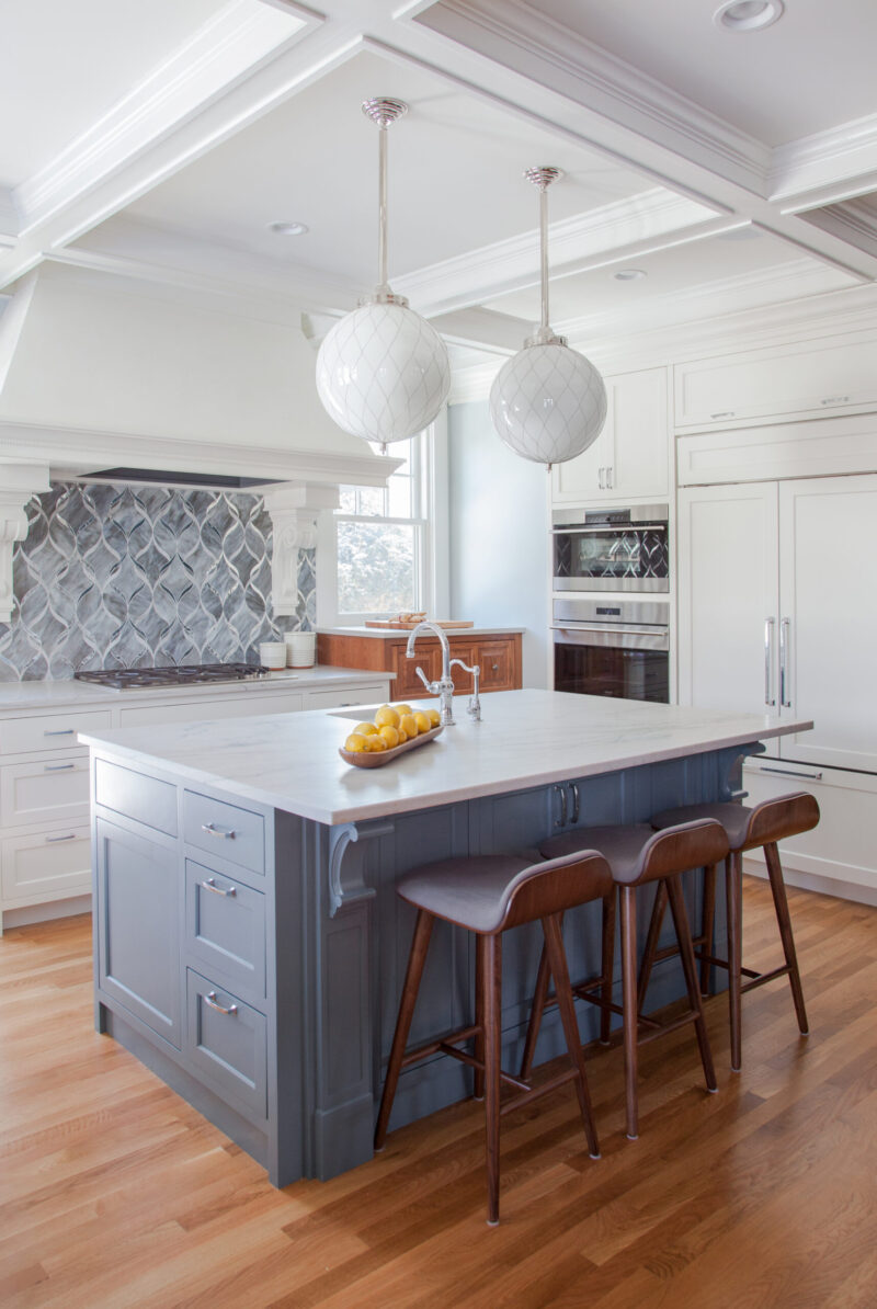 Kitchen remodel boasts white cabinetry, gray island, intricate backsplash.