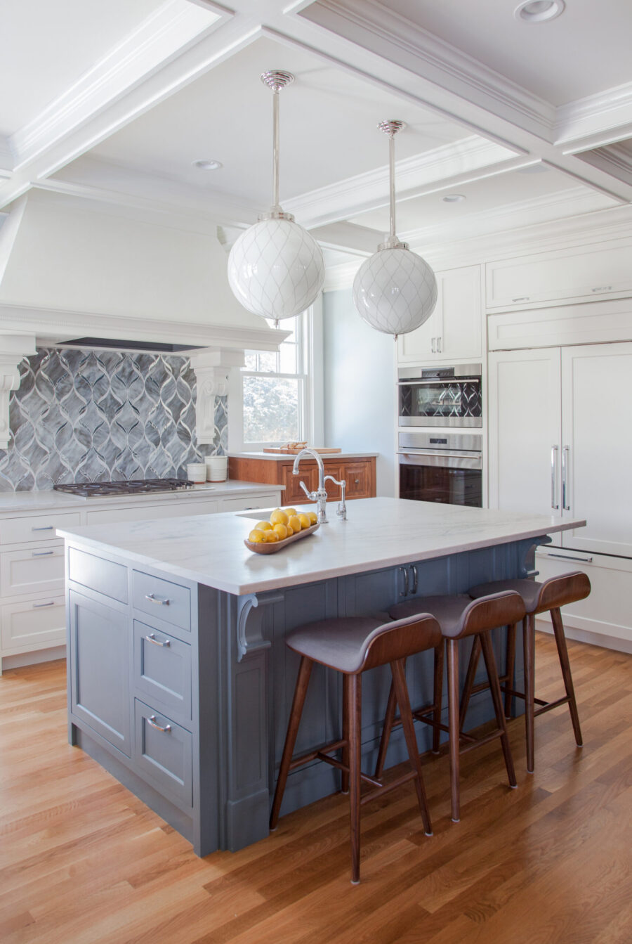 Kitchen remodel boasts white cabinetry, gray island, intricate backsplash.