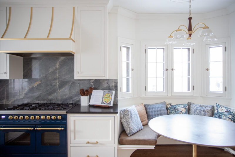 A bright Twin Cities kitchen remodel features a blue range, marble backsplash, white cabinetry, and bay window dining nook.