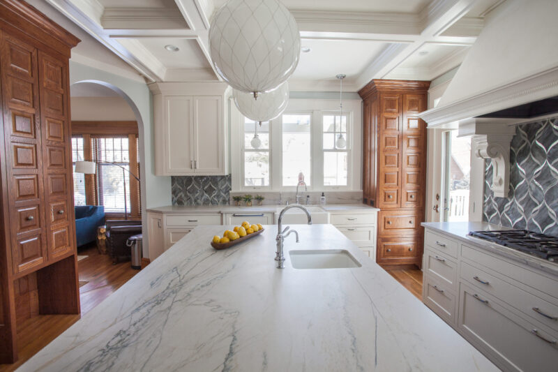 Twin Cities kitchen features marble island, white cabinets, dark wood pantry, and a coffered ceiling.
