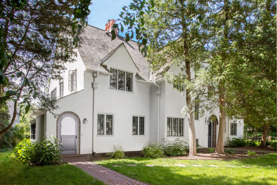 White stucco home renovation; black windows, arched brick entries, mature green landscaping.